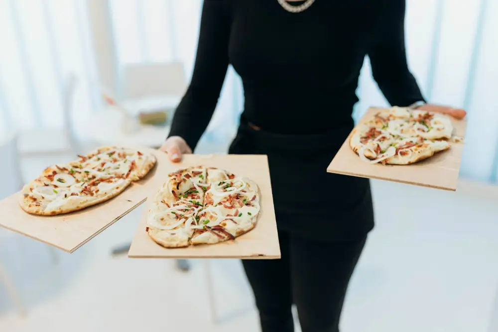 Servicekraft trägt drei Flammkuchen auf Holzbrettern