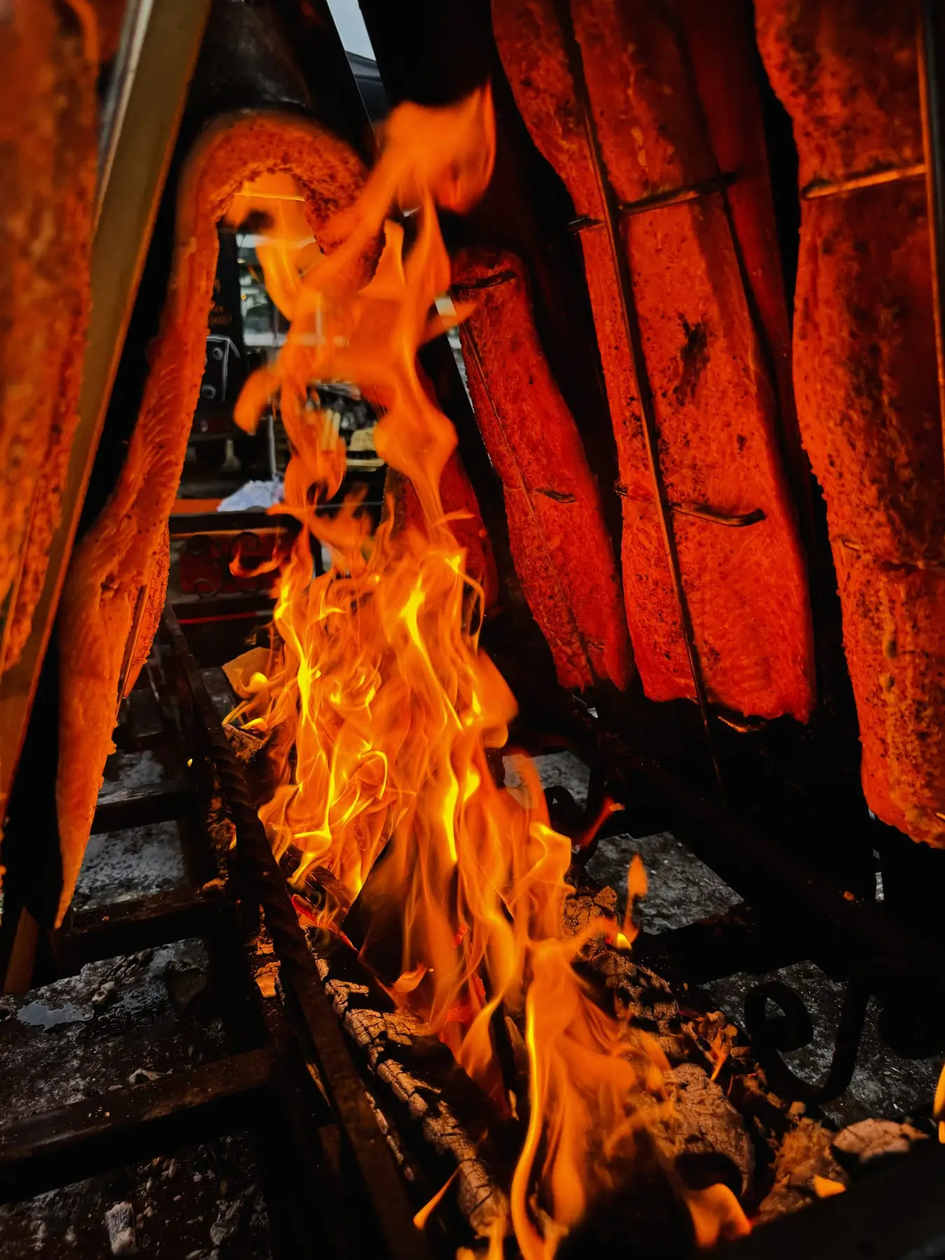 Lachsseiten auf Holzbrettern garen am offenen Buchenholzfeuer